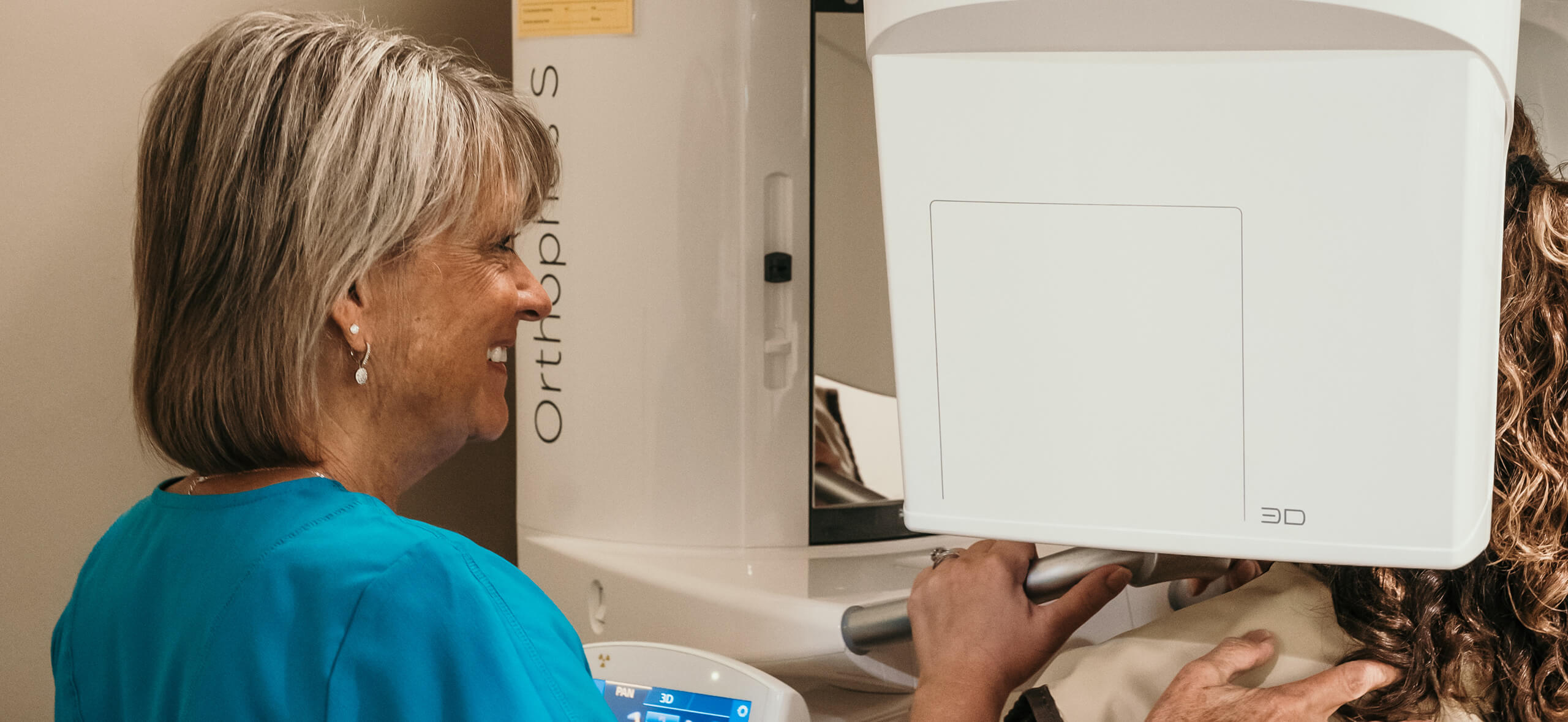 A dental assistant operates a 3D imaging scanner while a patient undergoes a dental X-ray