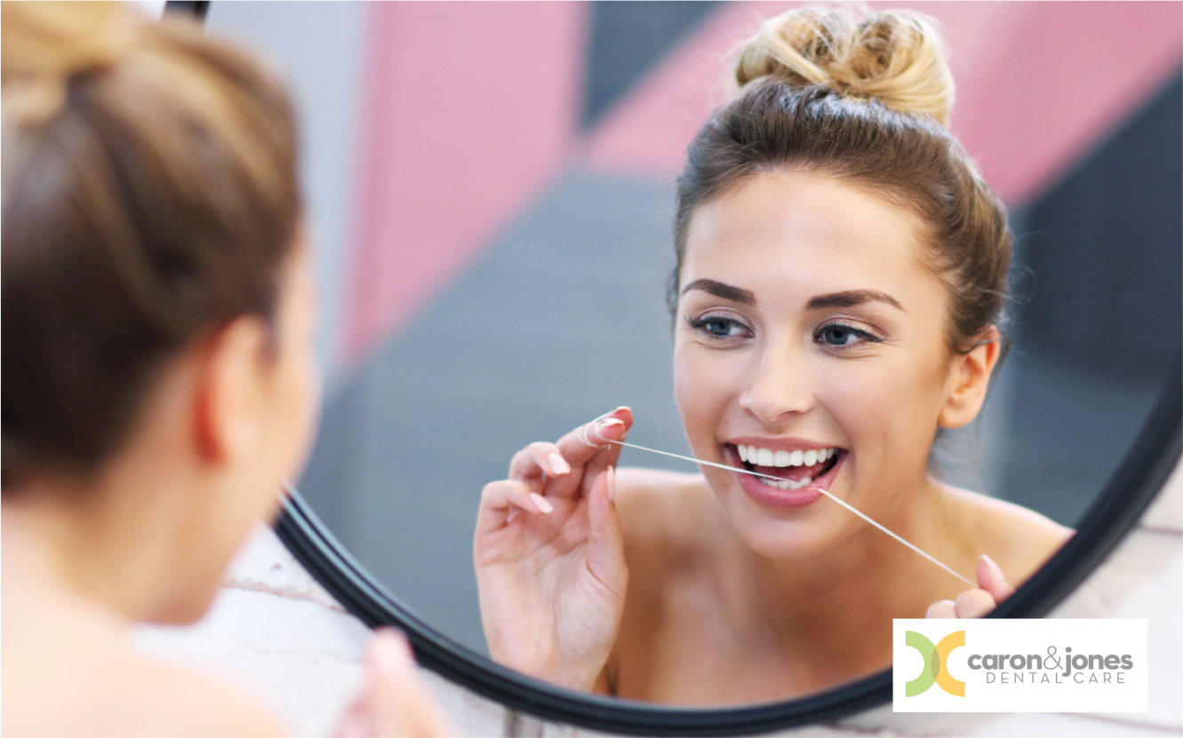 Woman flossing teeth in front of bathroom mirror for oral hygiene