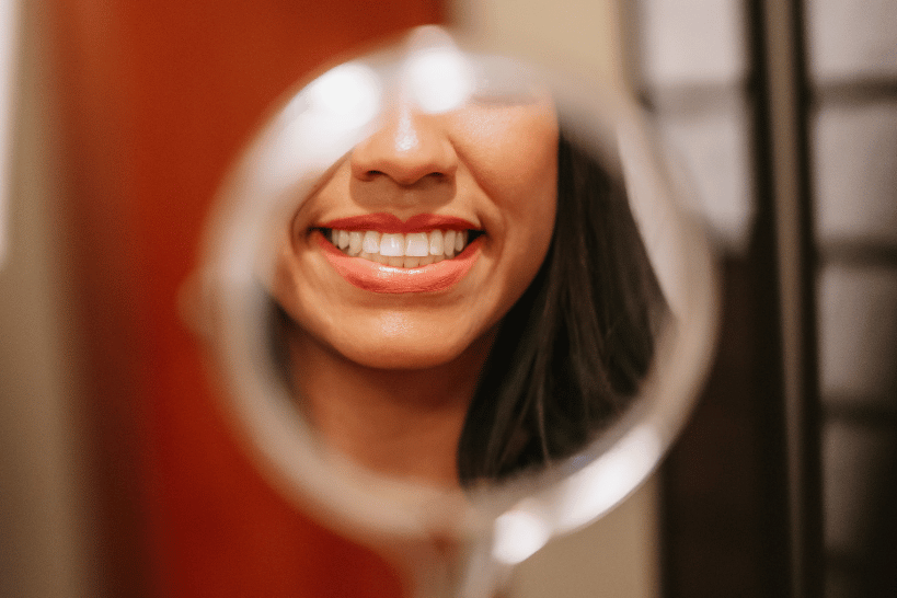 Woman smiling brightly while viewing teeth in mirror.
