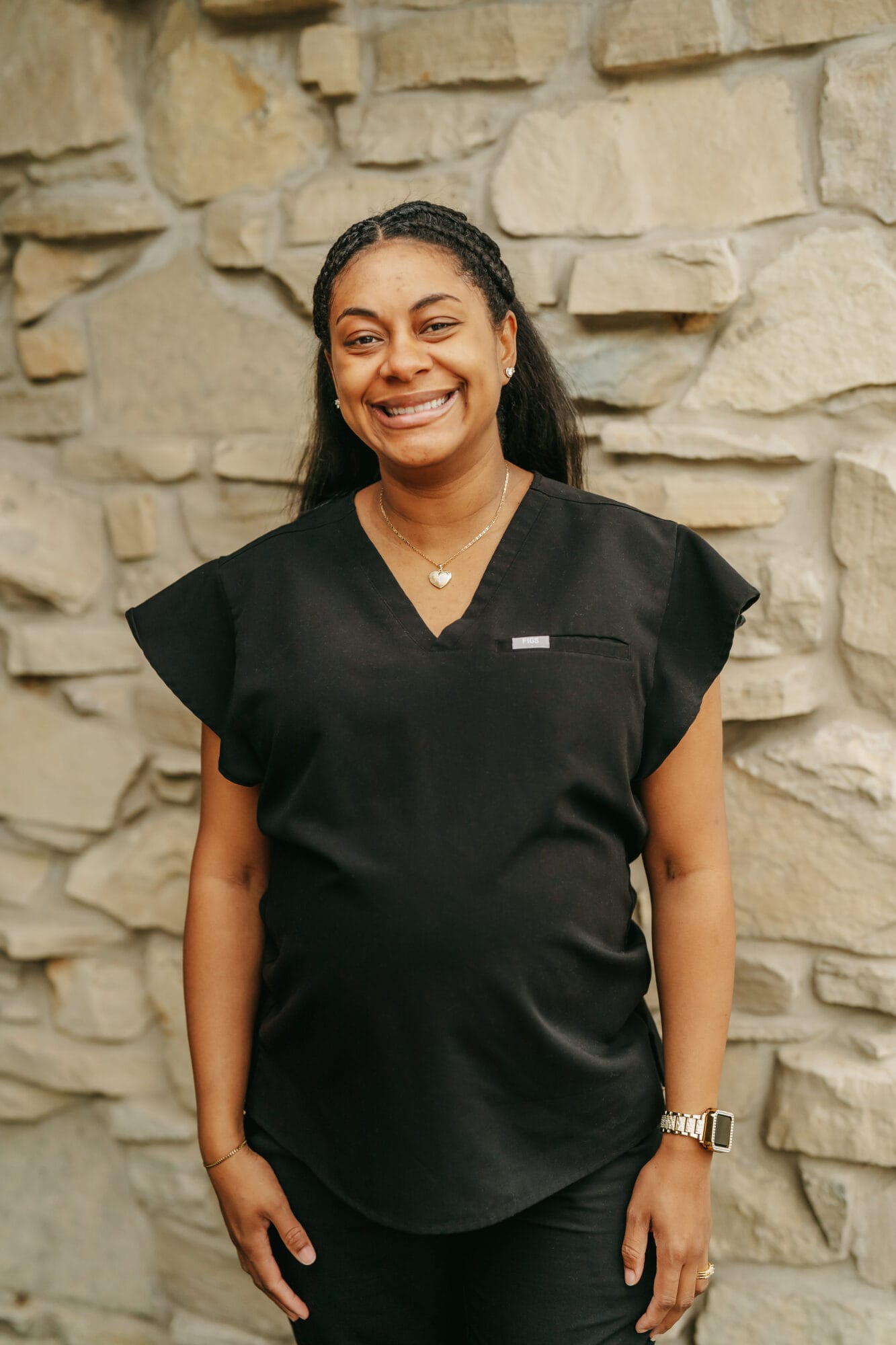 Headshot of Morgan Kiser, Dental Assistant with braided hair smiles at the camera while wearing black scrubs, conveying a caring and approachable dental team atmosphere