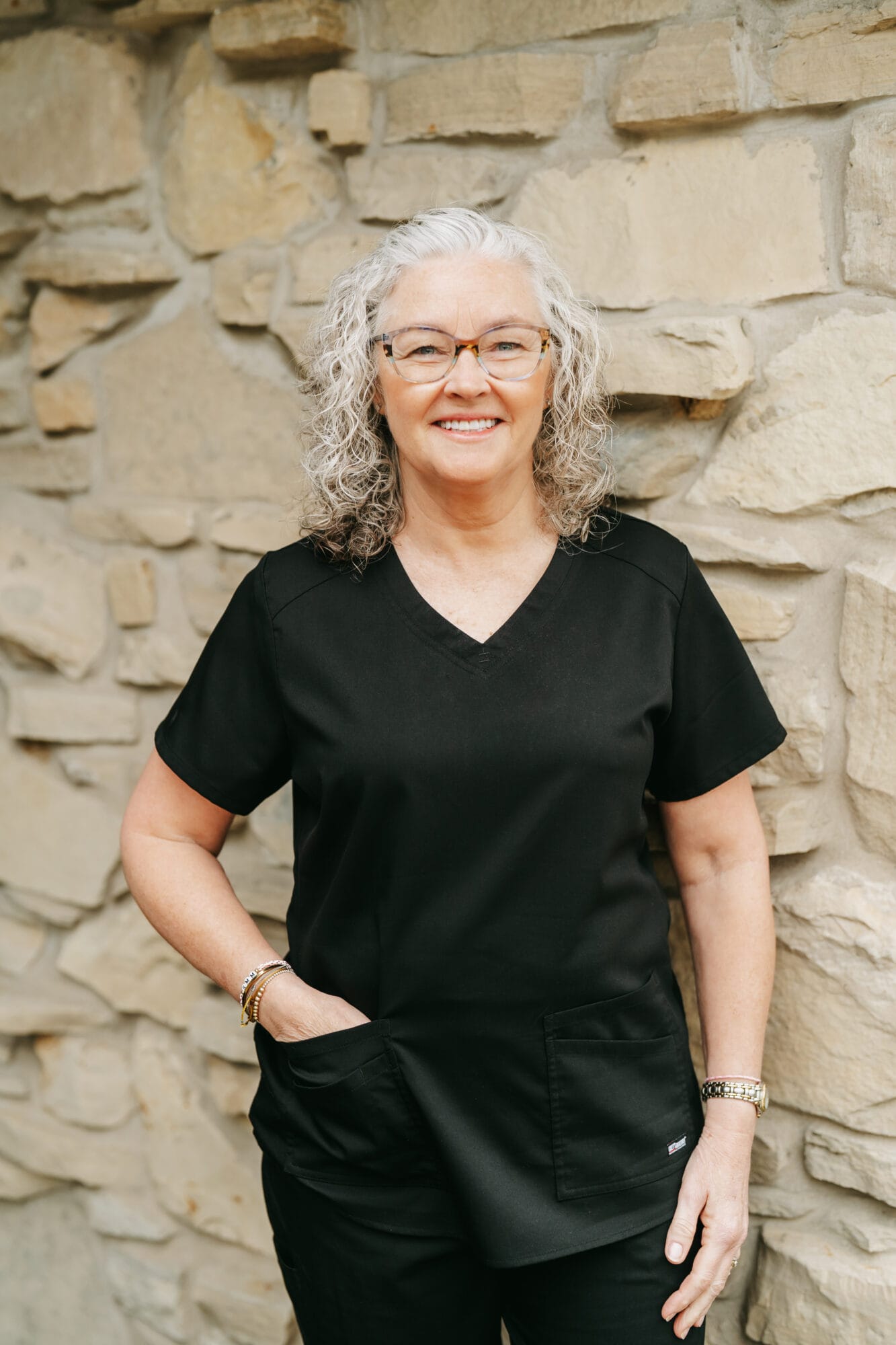 Headshot of Susan Meissnest, Dental Hygienist with gray curly hair and glasses smiles in the hallway of a dental clinic