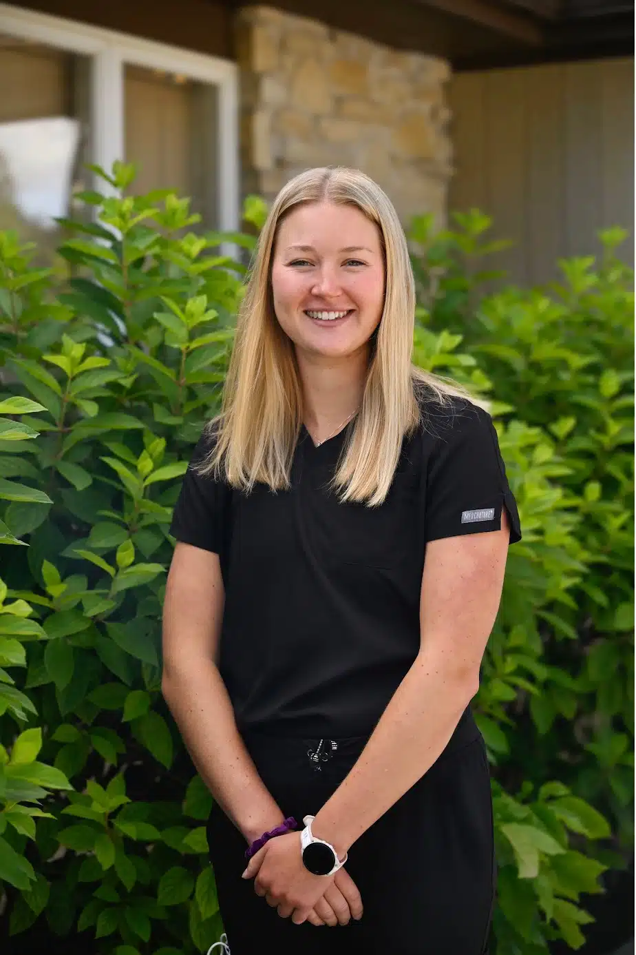 Headshot of Dr. Kayla Kirtley, D.D.S., MBA in black scrubs smiles warmly while standing outside the dental office